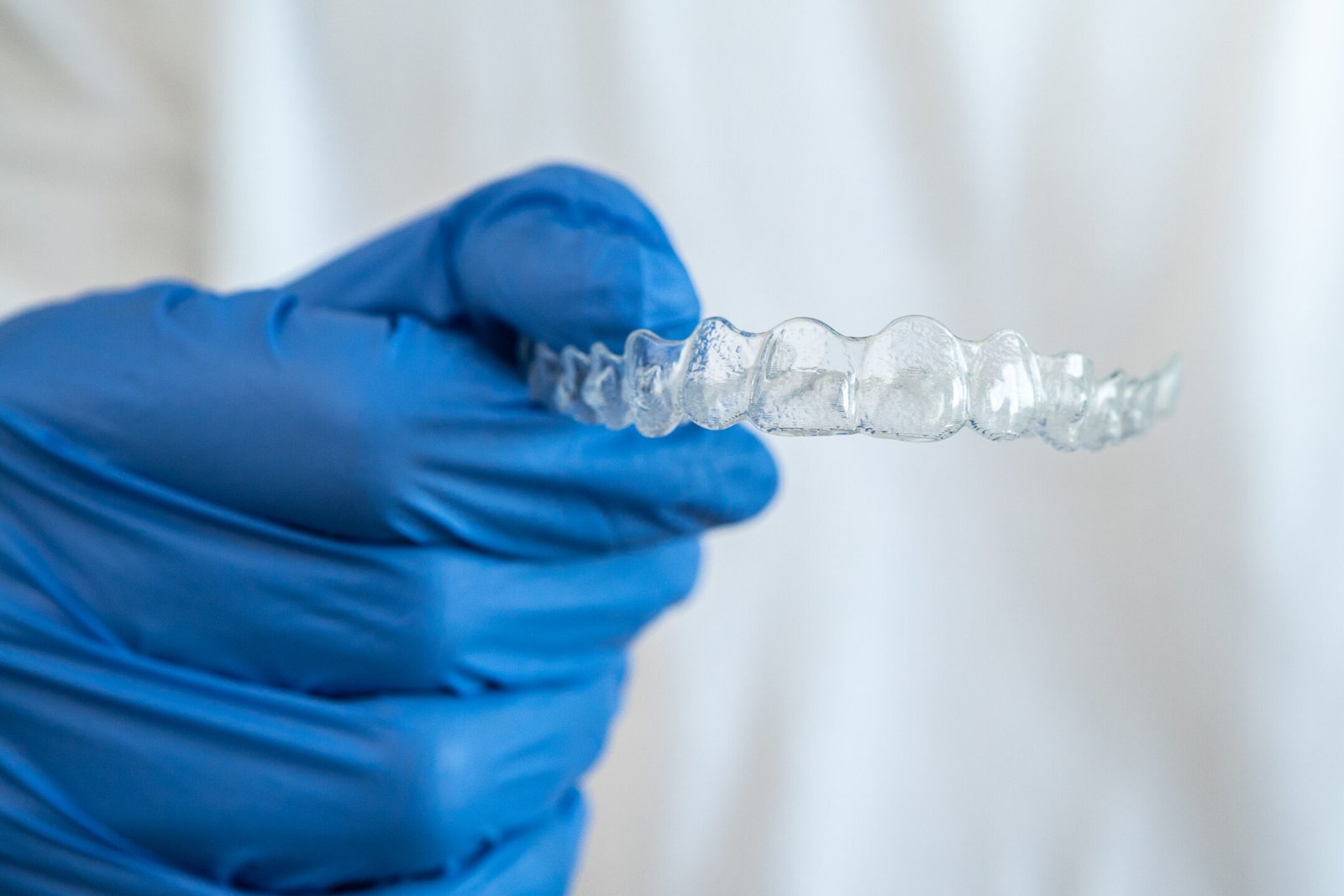 Male hand in gloves holding dental aligner retainer on white background of dental clinic for beautiful teeth treatment. Orthodontic removable straighteners in dentist office